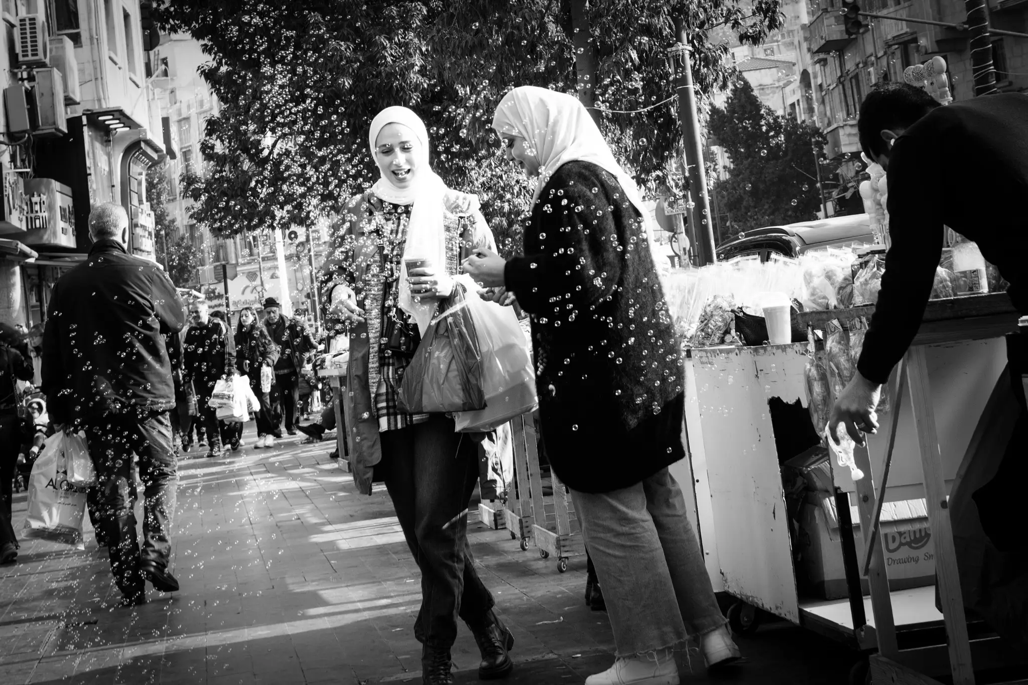 Due donne sorridono tra le bolle di sapone in una strada affollata di Amman