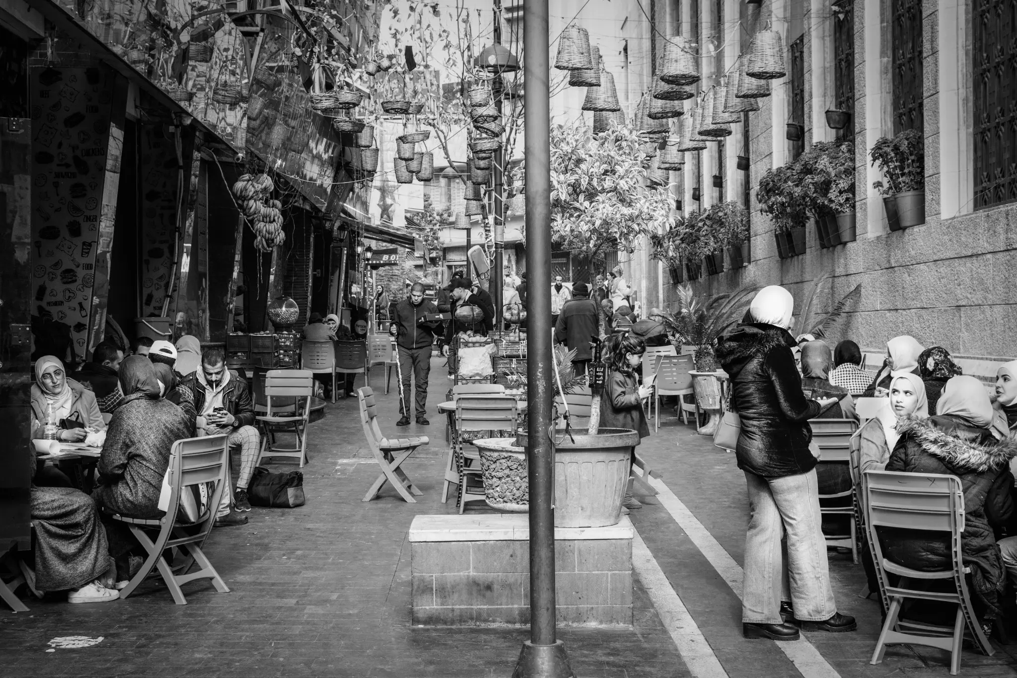 Una via di Amman piena di tavolini, caffè e persone sedute.