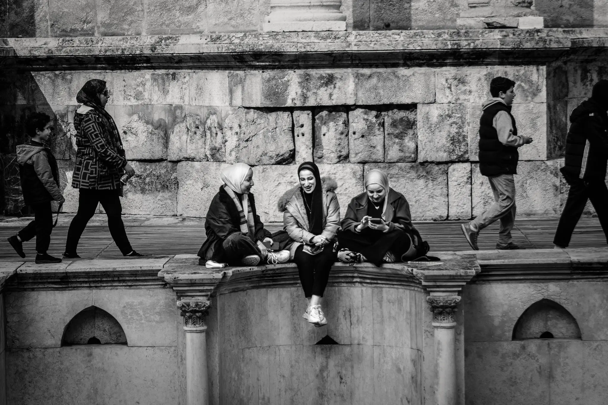 Tre ragazze sorridono sedute sulle gradinate in pietra del teatro romano di Amman.