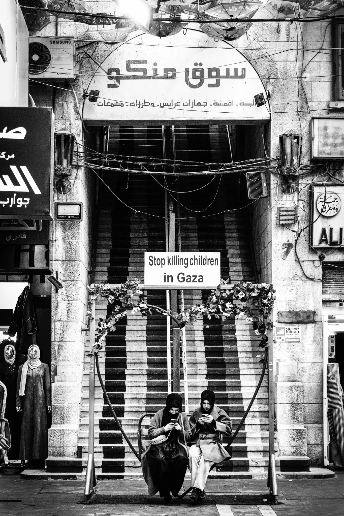 Due giovani donne siedono sotto un cartello con la scritta Stop killing children in Gaza.