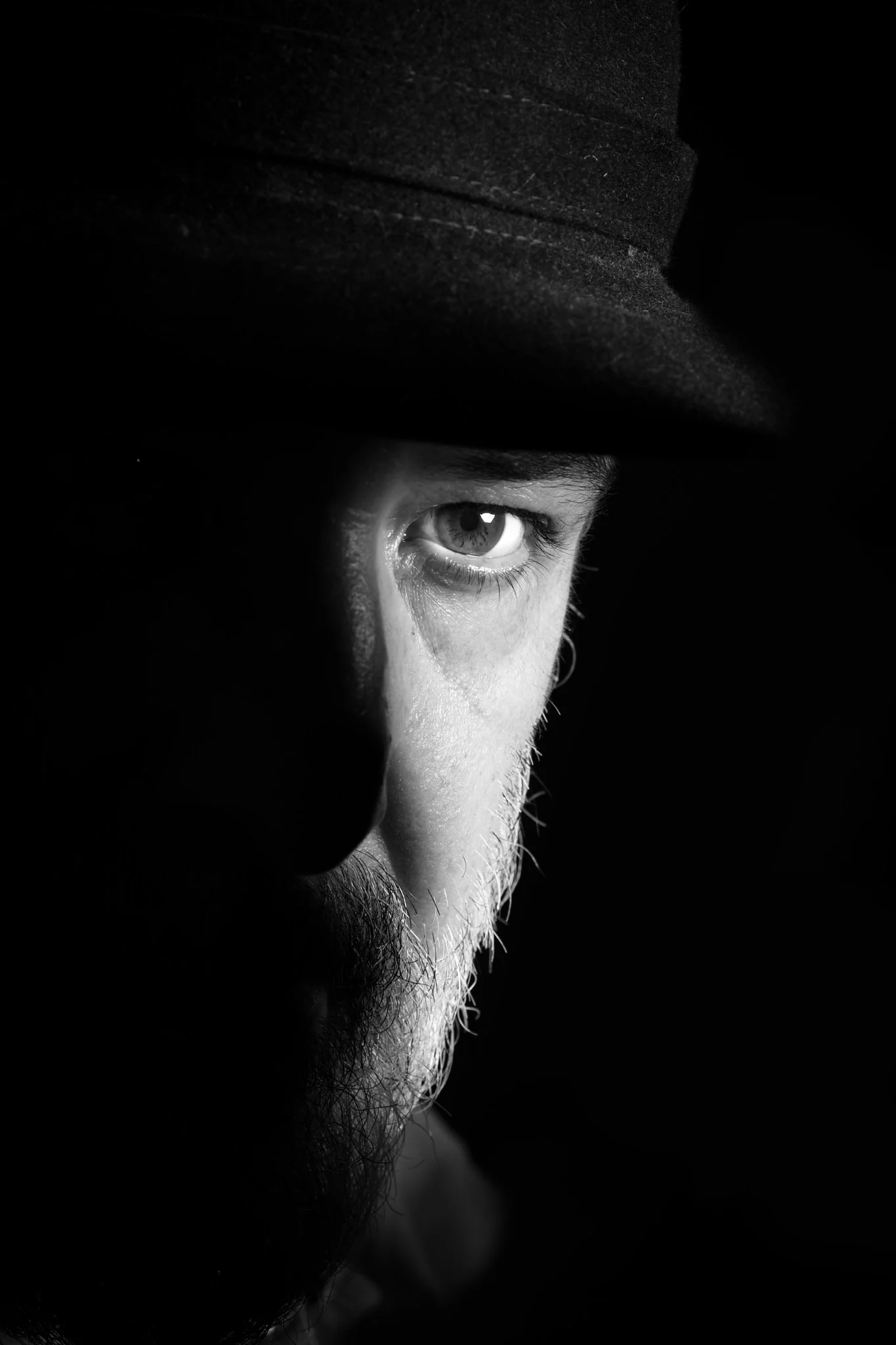 Ritratto in bianco e nero con un occhio incorniciato dalla mano e dal cappello
