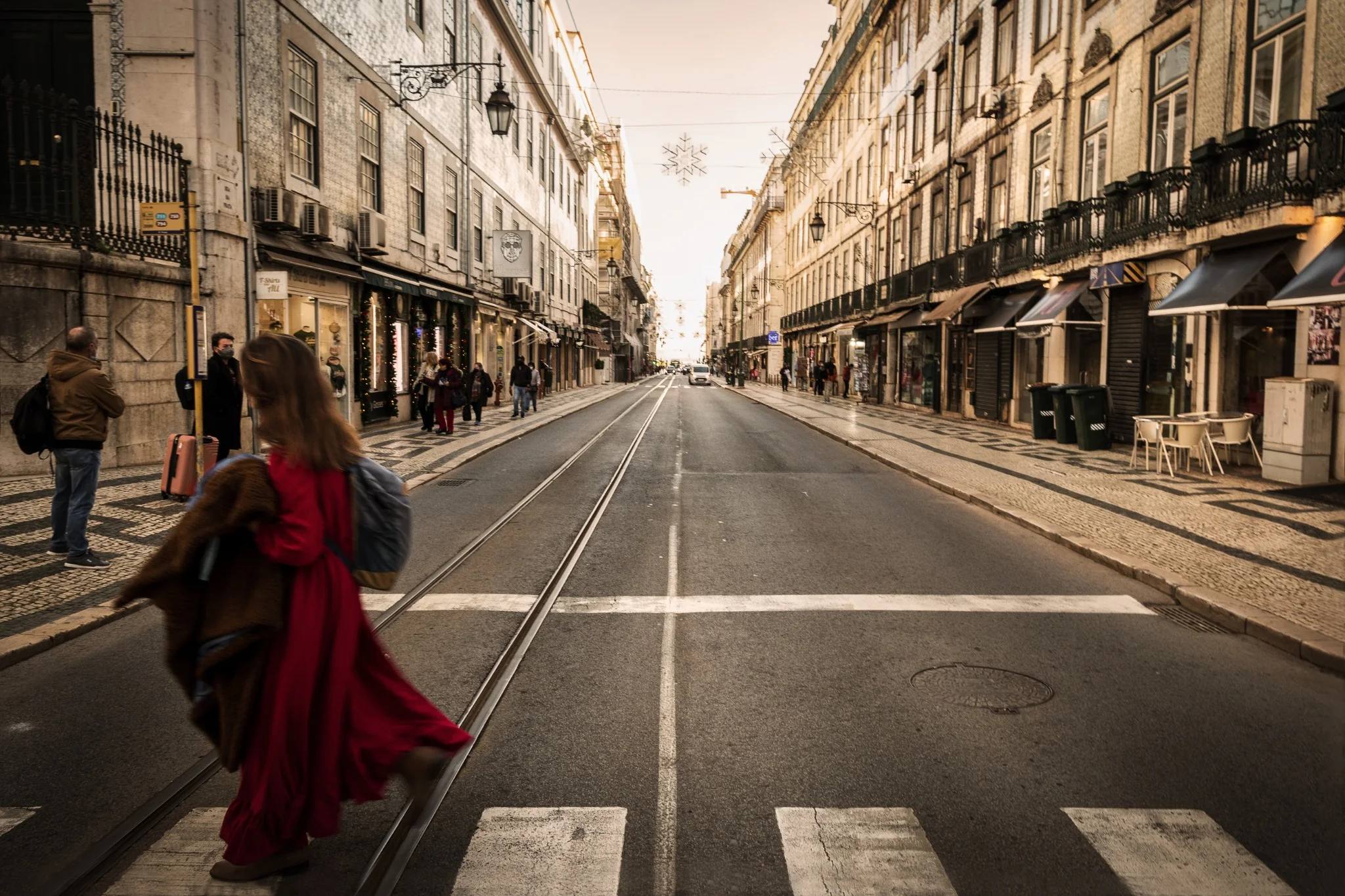 Una donna vestita di rosso attraversa una strada di Lisbona davanti a un tram giallo e a un murale.