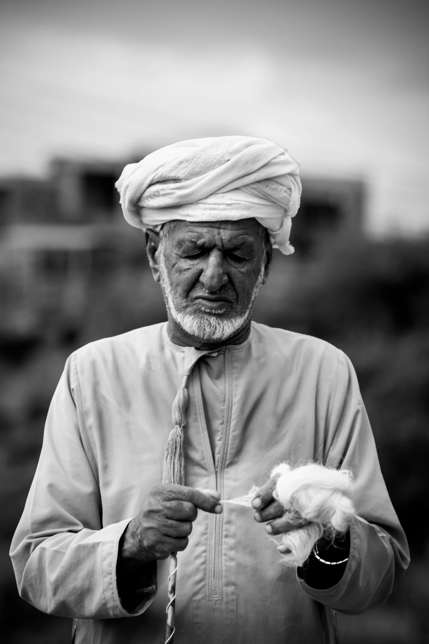 Un anziano omanita in abiti tradizionali lavora una fibra tessile a Jabal Shams.