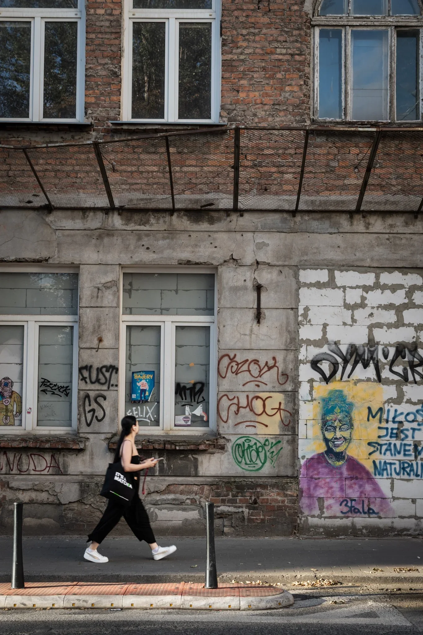 Una figura percorre uno spazio urbano tra muri, ombre e linee architettoniche a Cracovia.