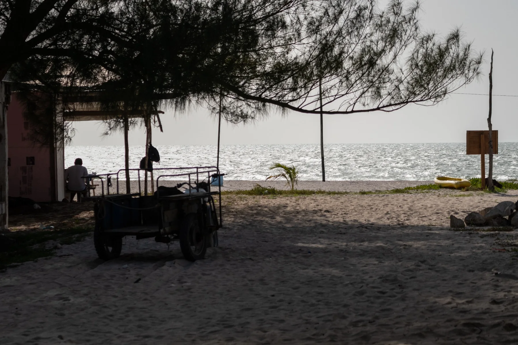 Spiaggia in controluce con una figura seduta sotto una tettoia
